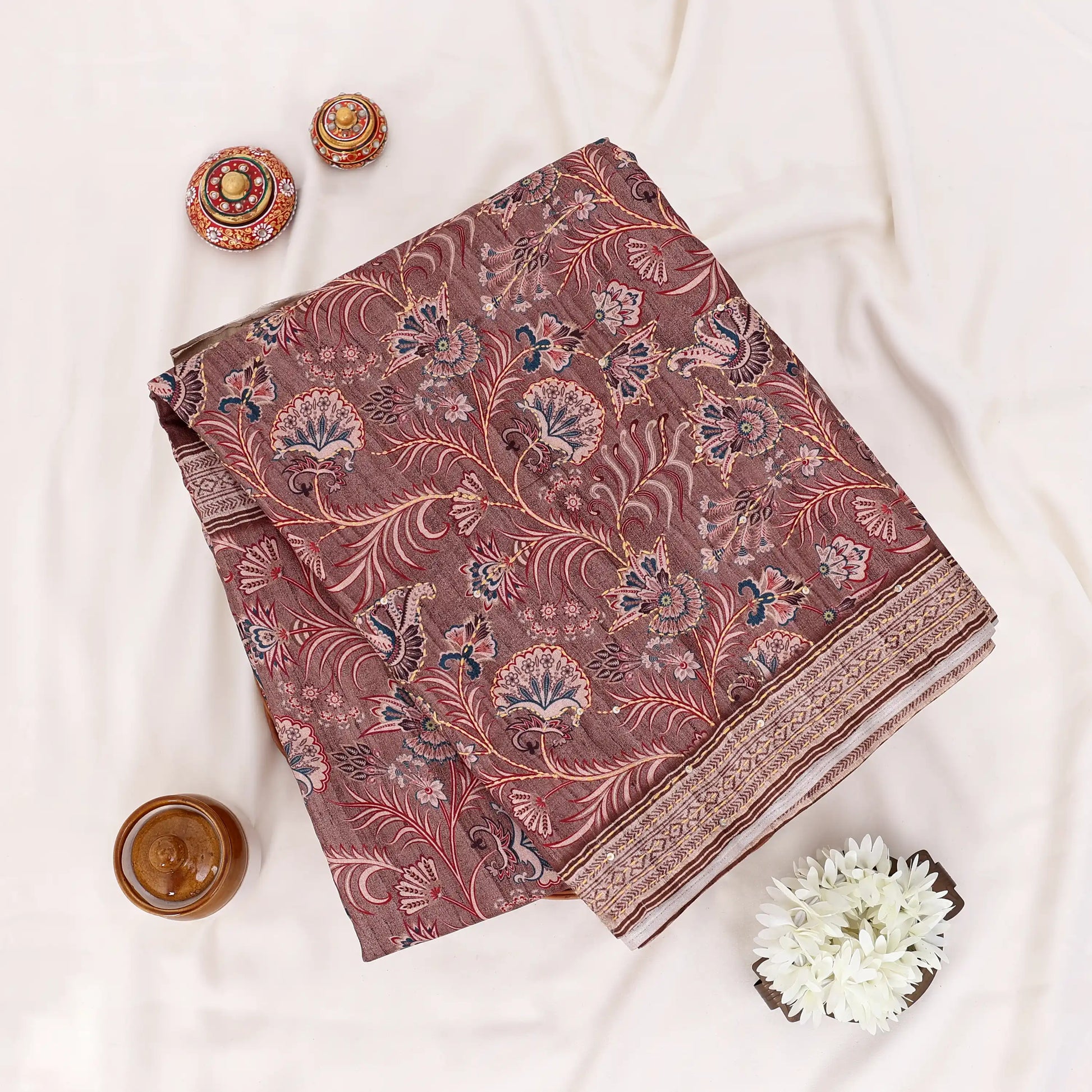 A folded deep brown saree with intricate gold and beige floral patterns