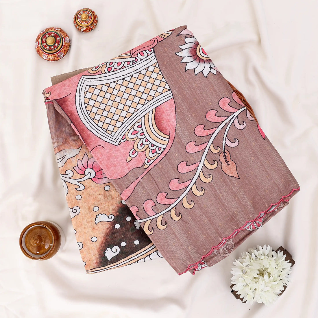 A brown saree with intricate floral and paisley patterns in pink, gold, and white