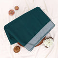 A folded dark teal green saree with a light gray border