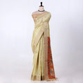 A light yellow saree draped featuring a wide beige border and a red patterned pallu