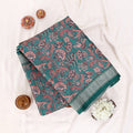 A folded dark green saree with intricate red and pink floral patterns and a striped border