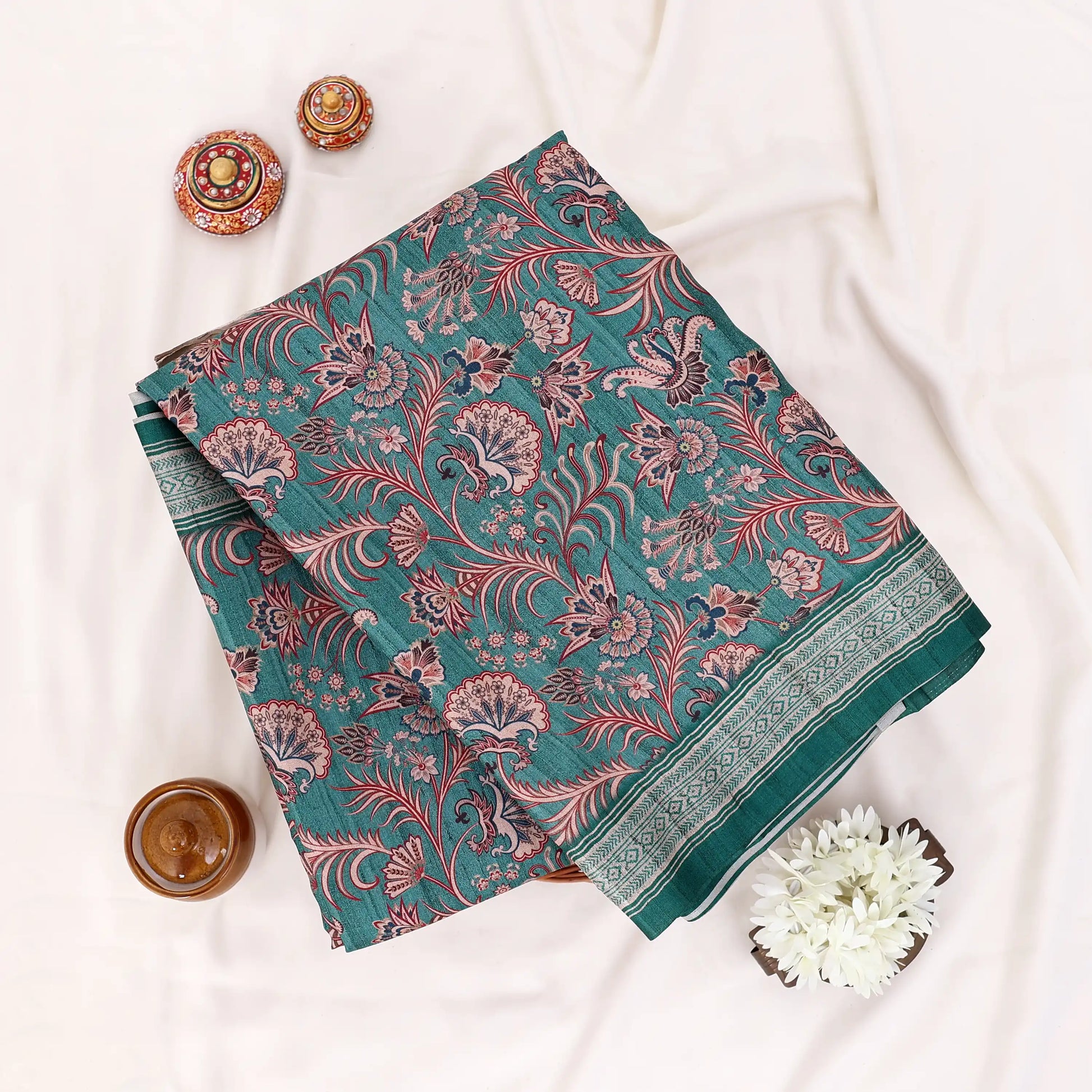 A folded dark green saree with intricate red and pink floral patterns and a striped border