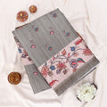 A folded gray saree with a pink border featuring colorful floral and bird motifs
