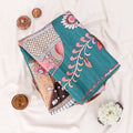 A folded teal sareewith  features a teal green base with pink floral and leaf patterns, alongside brown, beige, and white geometric and floral motifs.