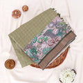 A folded green and brown printed saree features a sage green body with brown borders and pink floral patterns.