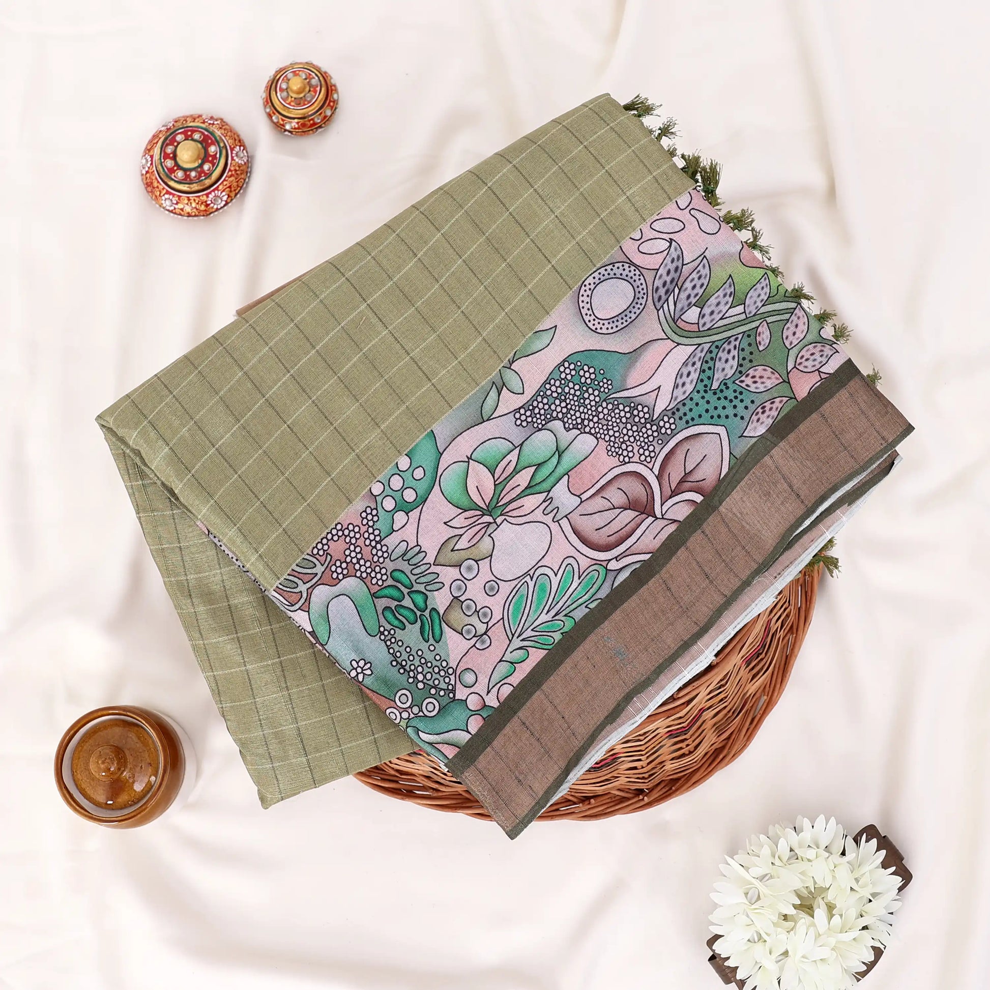 A folded green and brown printed saree features a sage green body with brown borders and pink floral patterns.