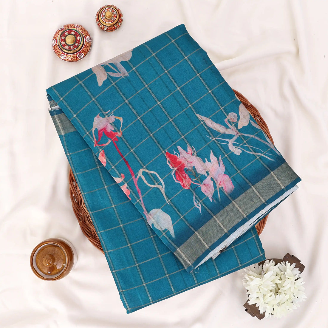 A teal blue saree with a subtle grid pattern and pink floral prints