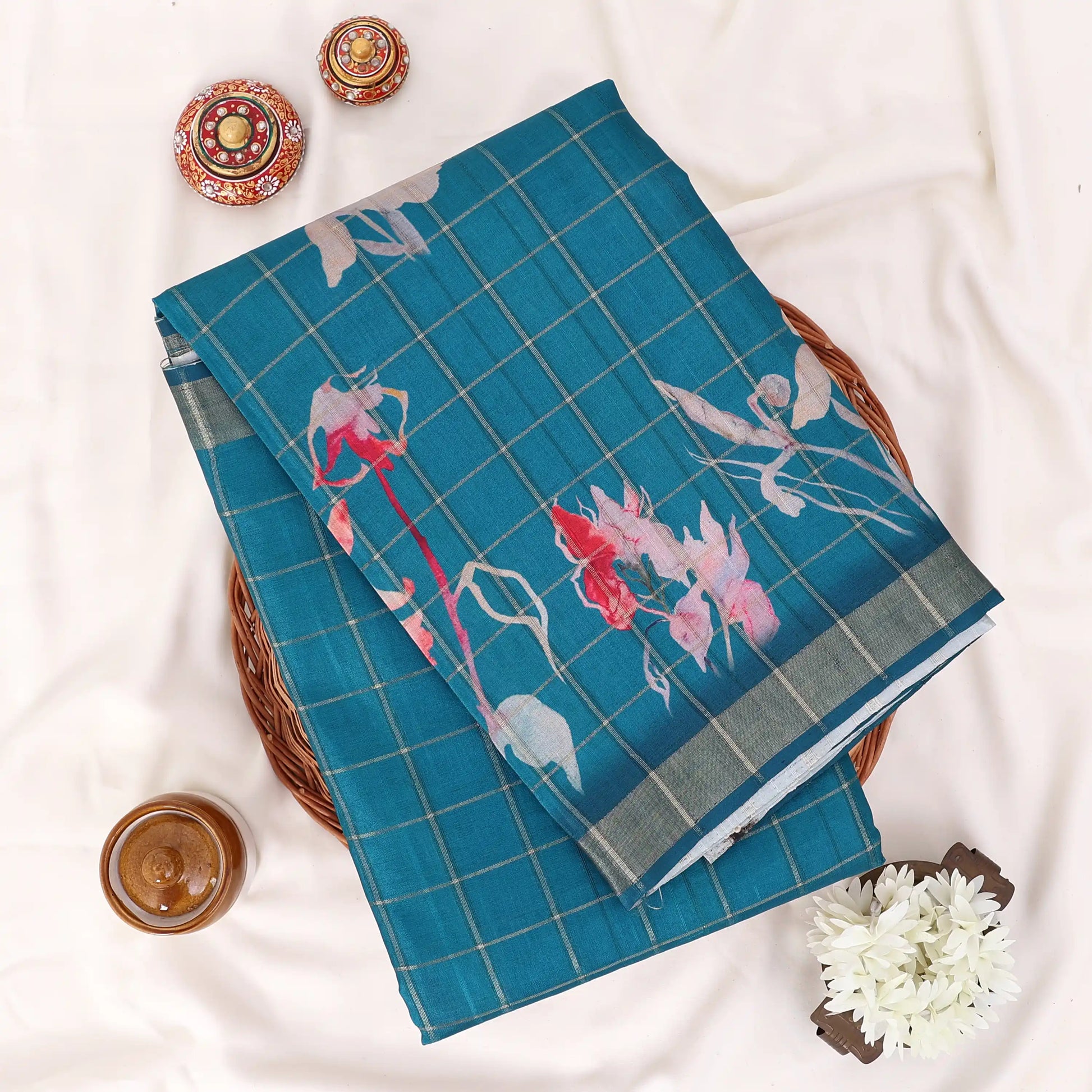 A folded teal blue saree with a grid pattern and pink, red, and white floral motifs