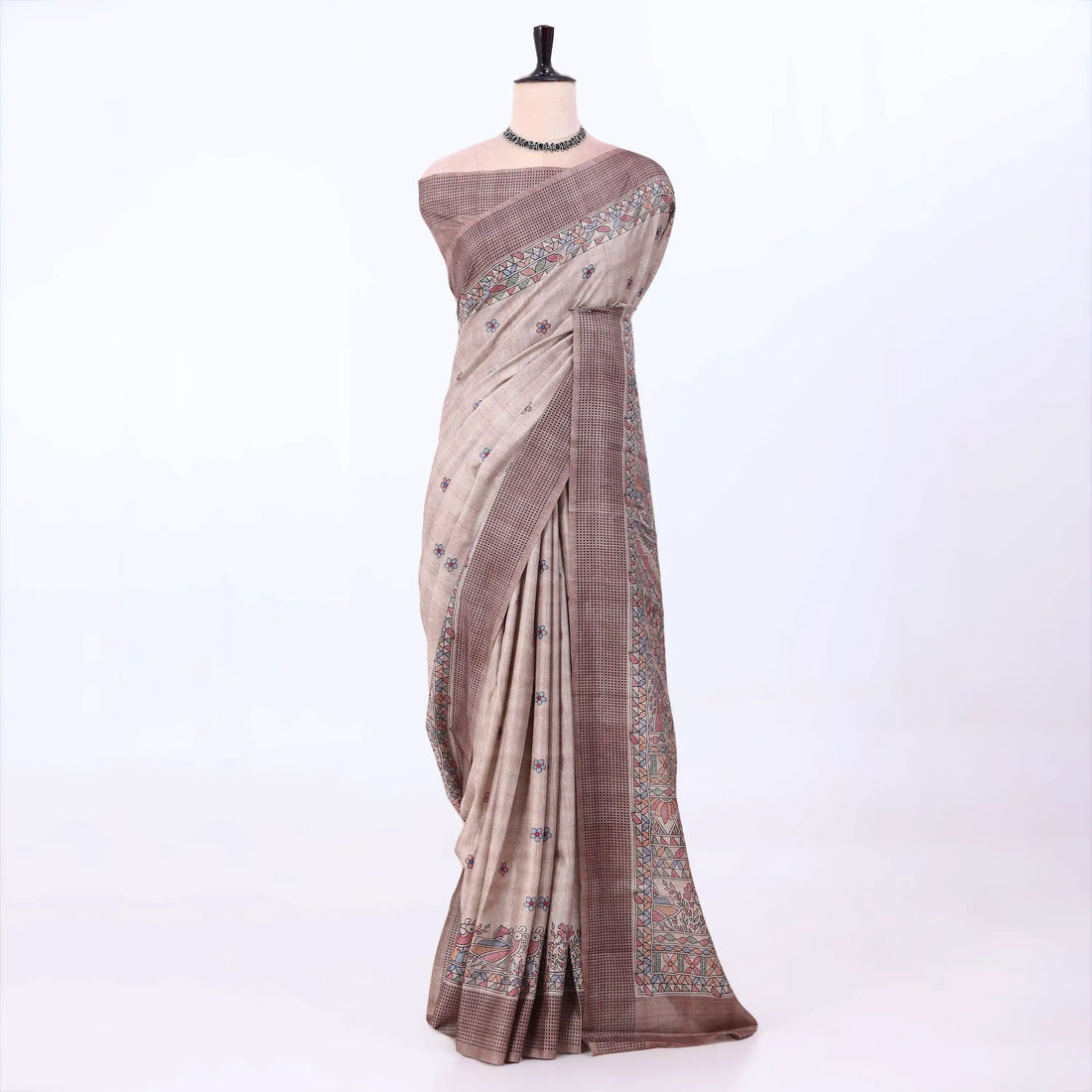 The saree has a warm taupe and brown base with a subtle plaid pattern and ornate multicolor border details in blue, red, and green.