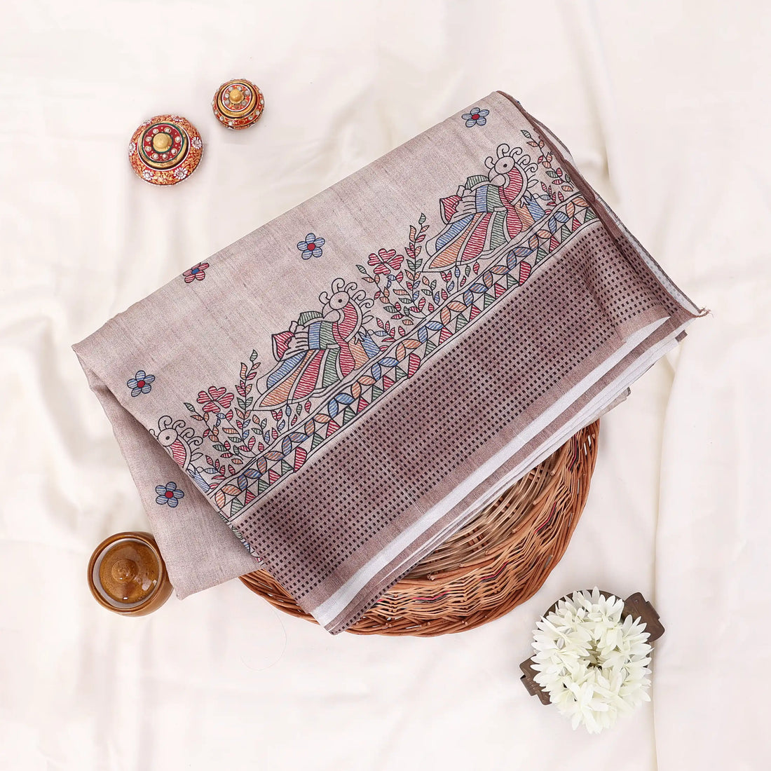 The saree has a warm taupe and brown base with a subtle plaid pattern and ornate multicolor border details in blue, red, and green.