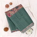 A folded dark green and black saree with a pink and multicolor printed border