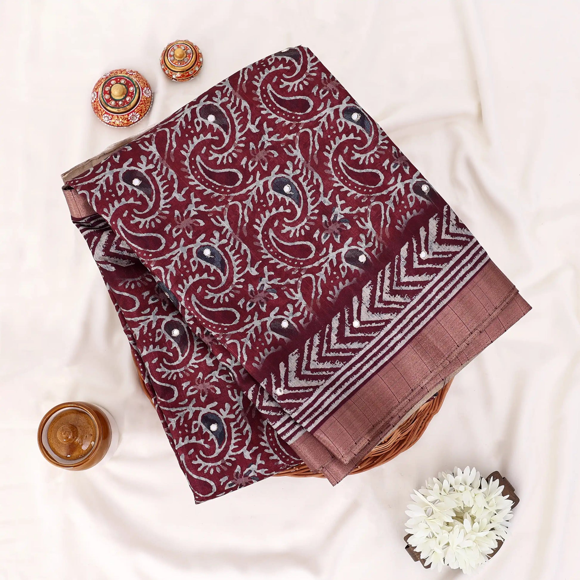 A folded piece of maroon paisley printed fabric with a striped border