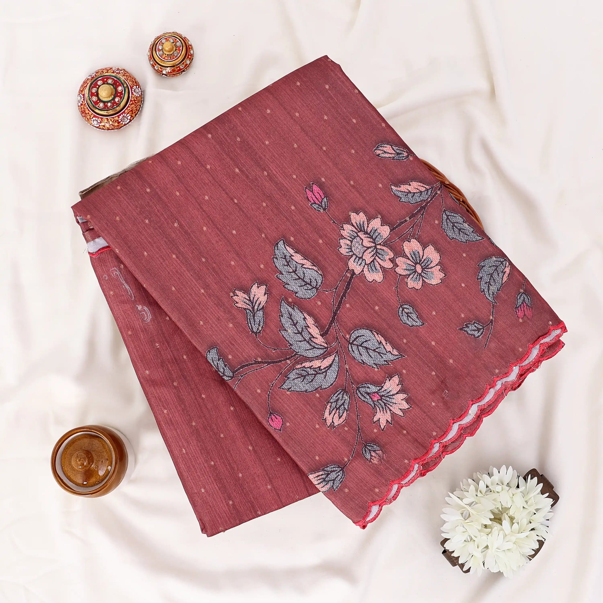 A folded terracotta red saree with a floral print in pink and gray