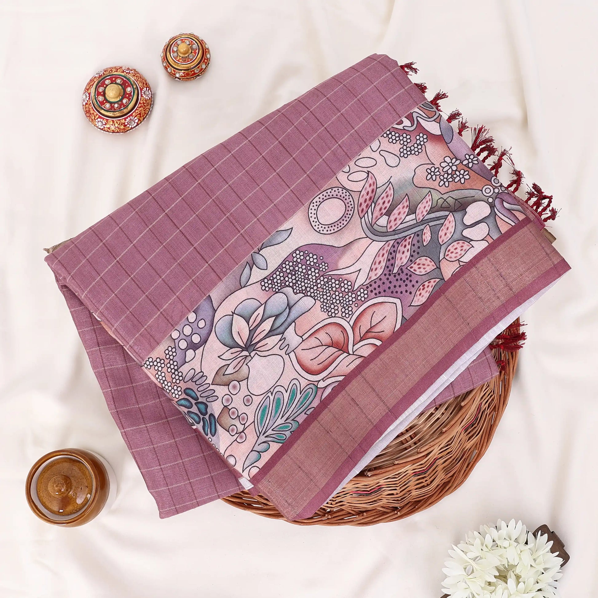 A folded mauve and pink patterned saree with features a solid mauve border, a floral printed pallu, and a matching printed blouse piece.