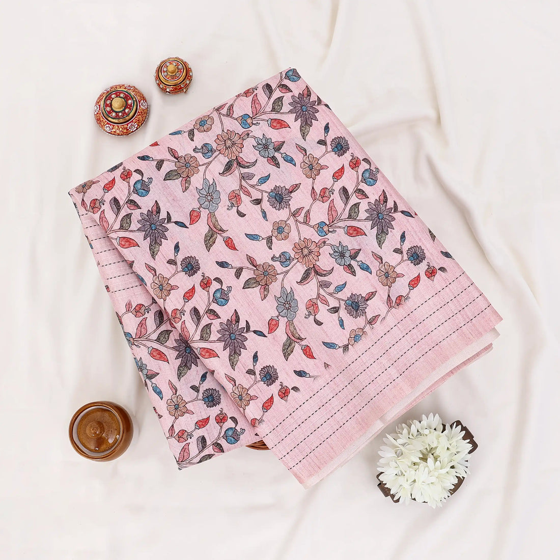 A pink saree with a subtle grid pattern and a floral print in muted blue, brown, and green