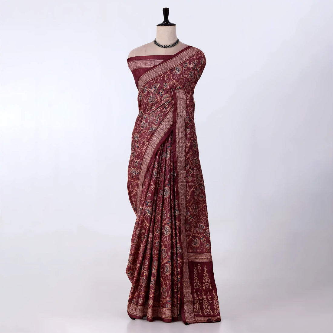 A deep maroon red saree with intricate gold and beige floral patterns