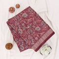 A folded deep maroon red saree with intricate gold and beige floral patterns