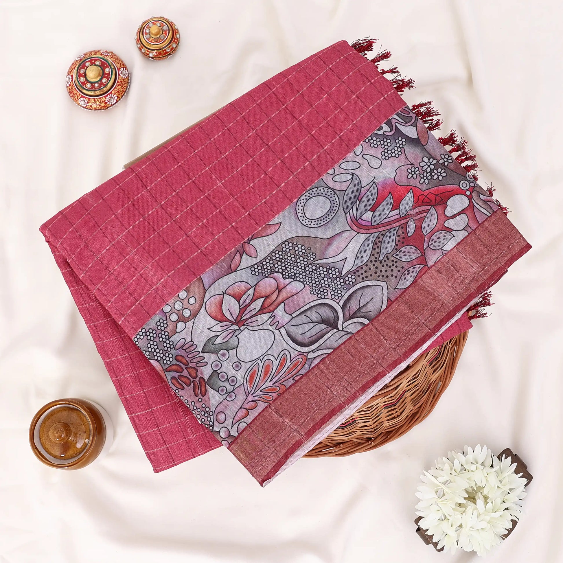 A folded red and grey printed saree features a sage red body with brown borders