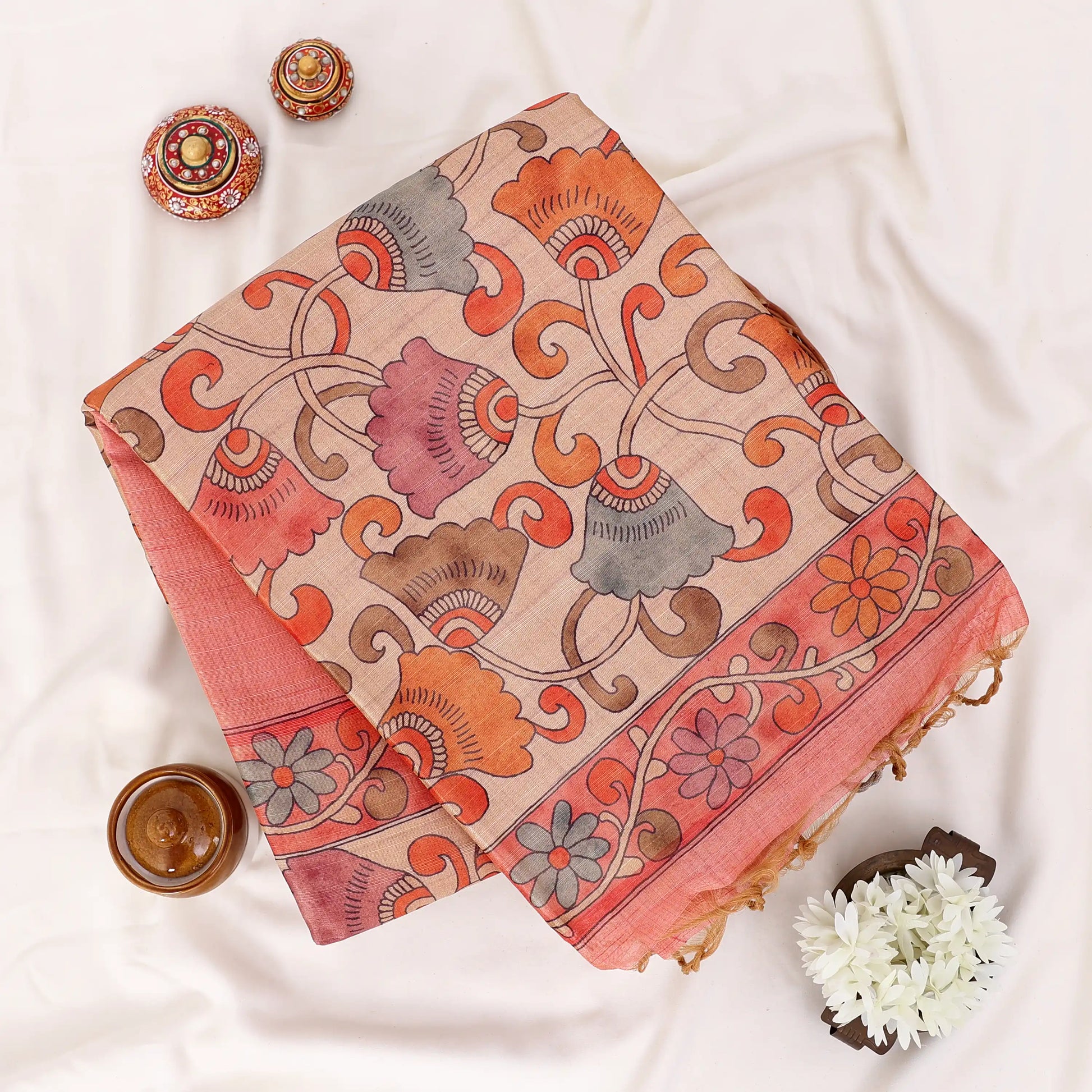 A folded peach-colored ilk saree with a beige border and a patterned orange and gold pallu