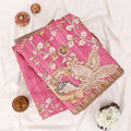 A folded pink saree with a detailed paisley and floral pattern in beige, brown, and white