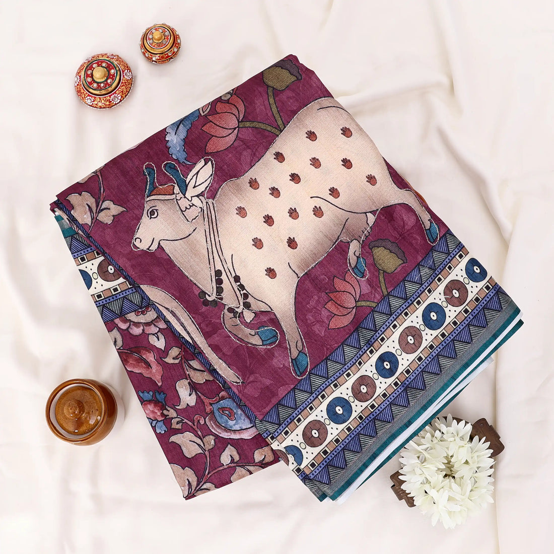 A multicolor printed saree features a deep maroon base with cream, teal, and gold patterns, including traditional motifs and striped borders.