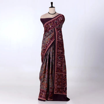 A dark plum purple saree with intricate red and gold floral patterns
