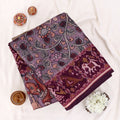 A folded dark plum purple saree with intricate red and gold floral patterns