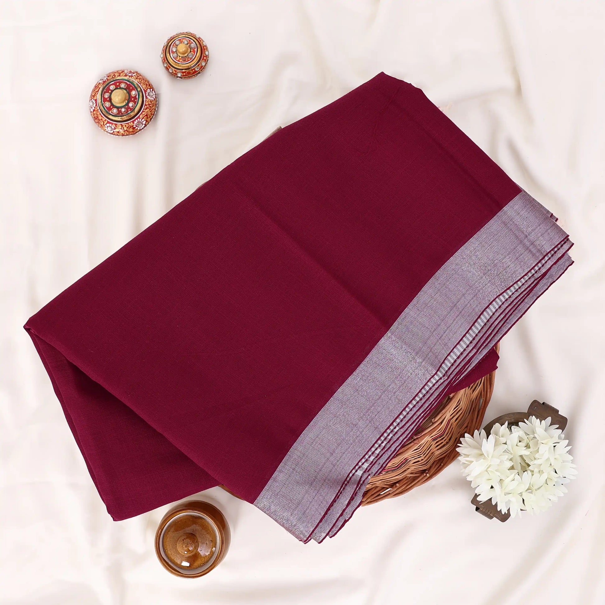 A folded deep maroon saree with a light gray border