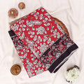 A folded red and black printed saree features a red base with black and white floral patterns and a solid black border. 