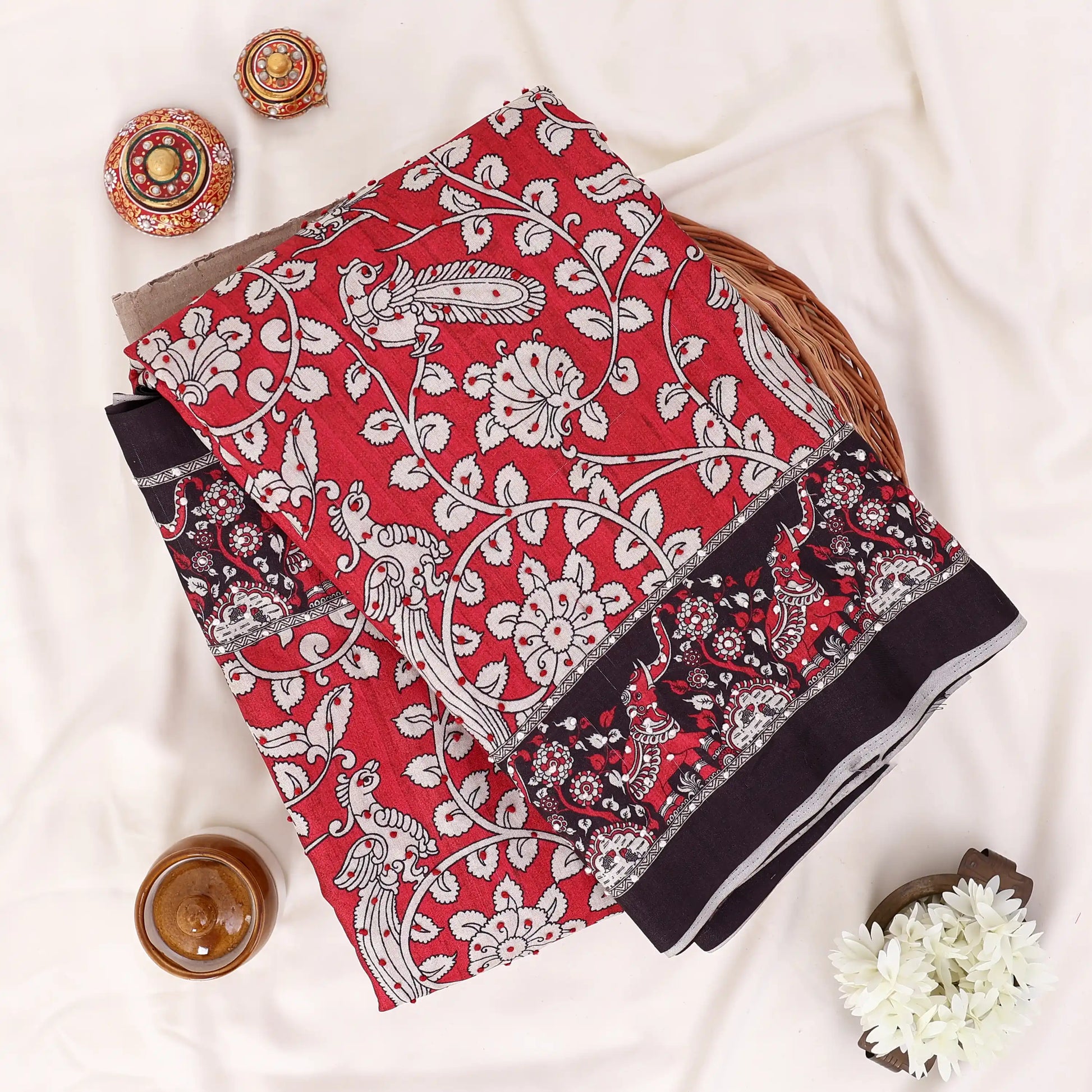 A folded red and black printed saree features a red base with black and white floral patterns and a solid black border. 
