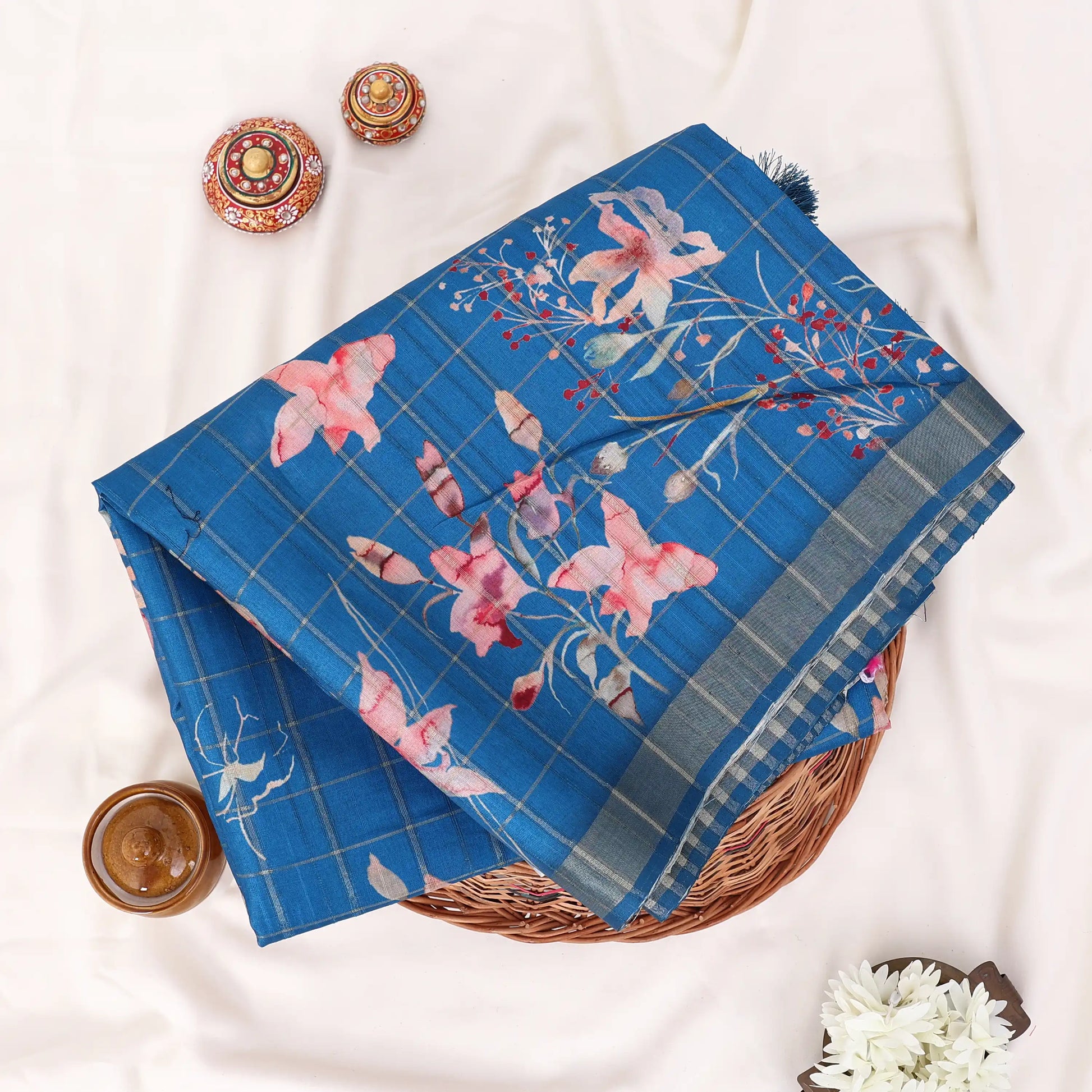 A folded blue patterned saree with pink floral motifs and a plaid border