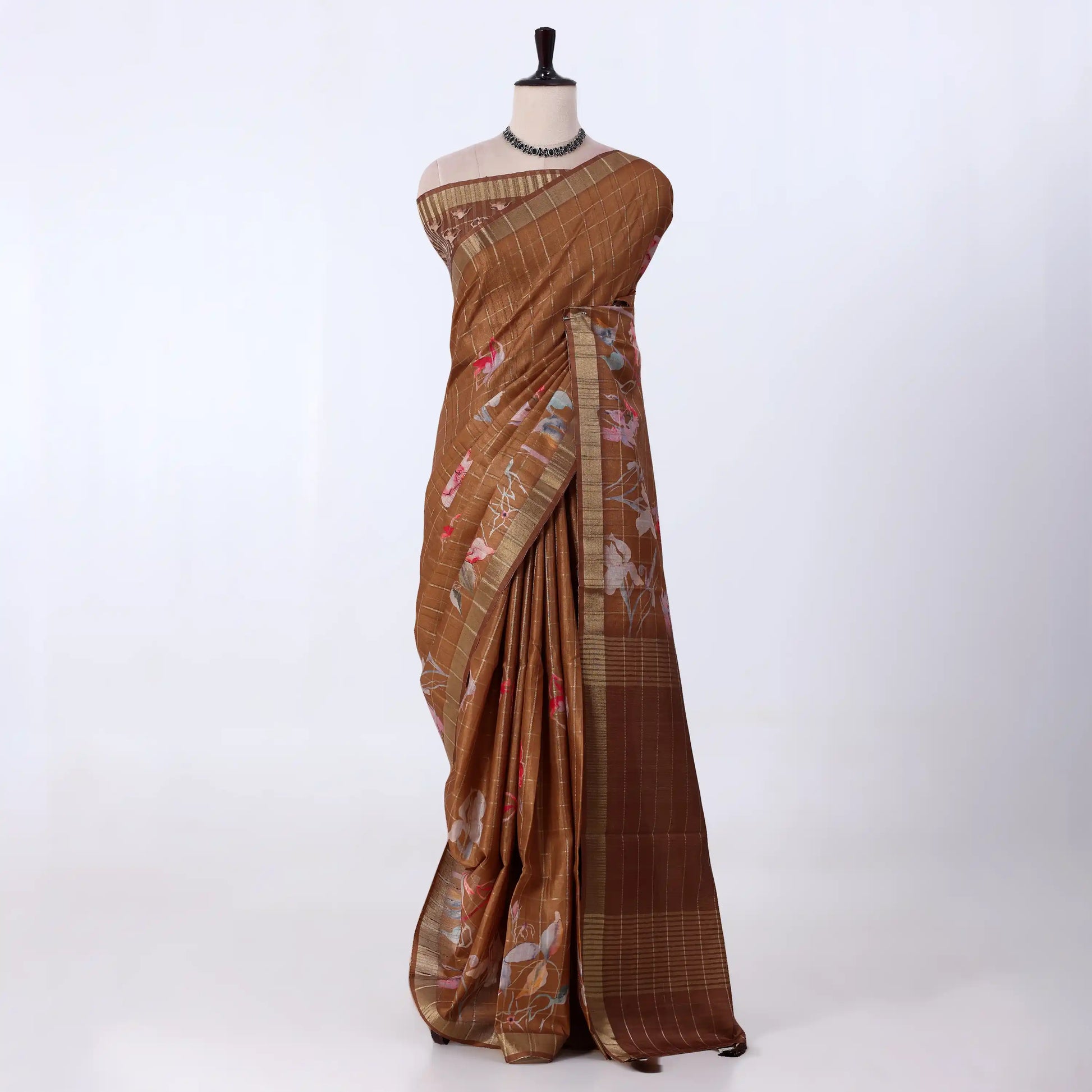 A brown tussar saree with floral prints and a striped border