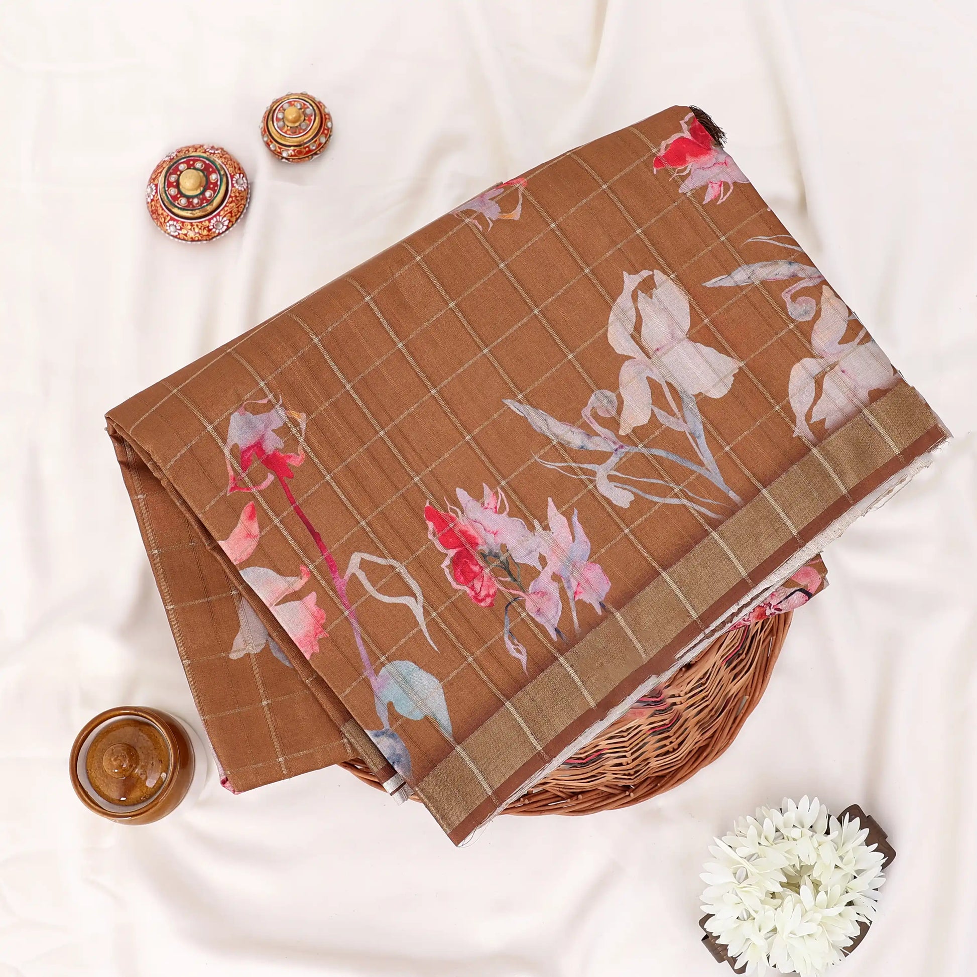 A folded brown tussar saree with floral prints and a striped border