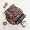 Art silk saree with intricate paisley floral print in black and gold woven border folded flat lay view in a wicker basket
