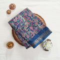 Art silk saree with intricate paisley floral print in blue and gold woven border folded flat lay view in a wicker basket