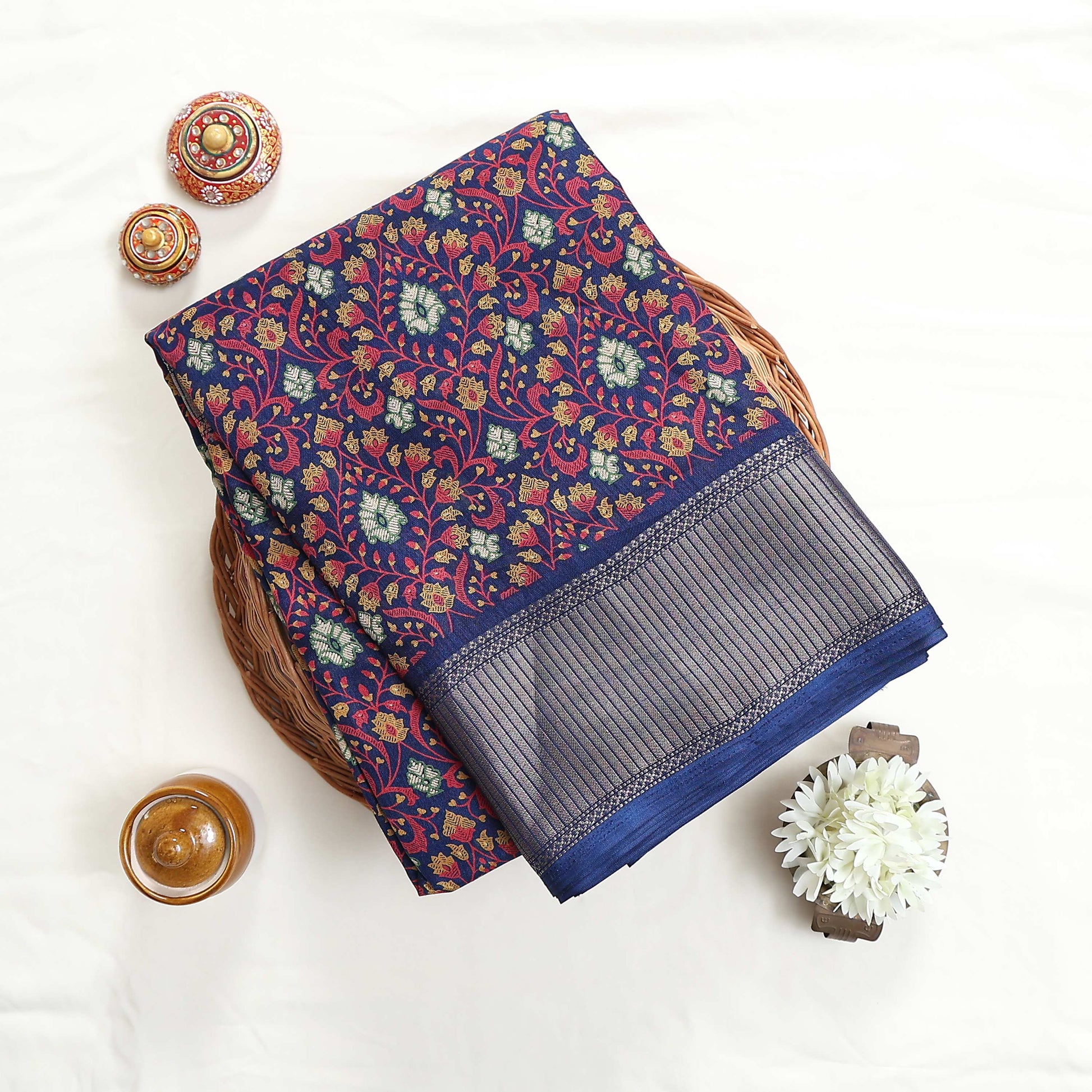 Art silk saree with floral vine jaal pattern and silver zari striped border in dark blue folded top view display