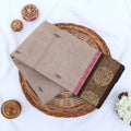 Chettinad cotton saree with floral zari border in beige and brown folded flat lay showcasing woven motifs and border detail.