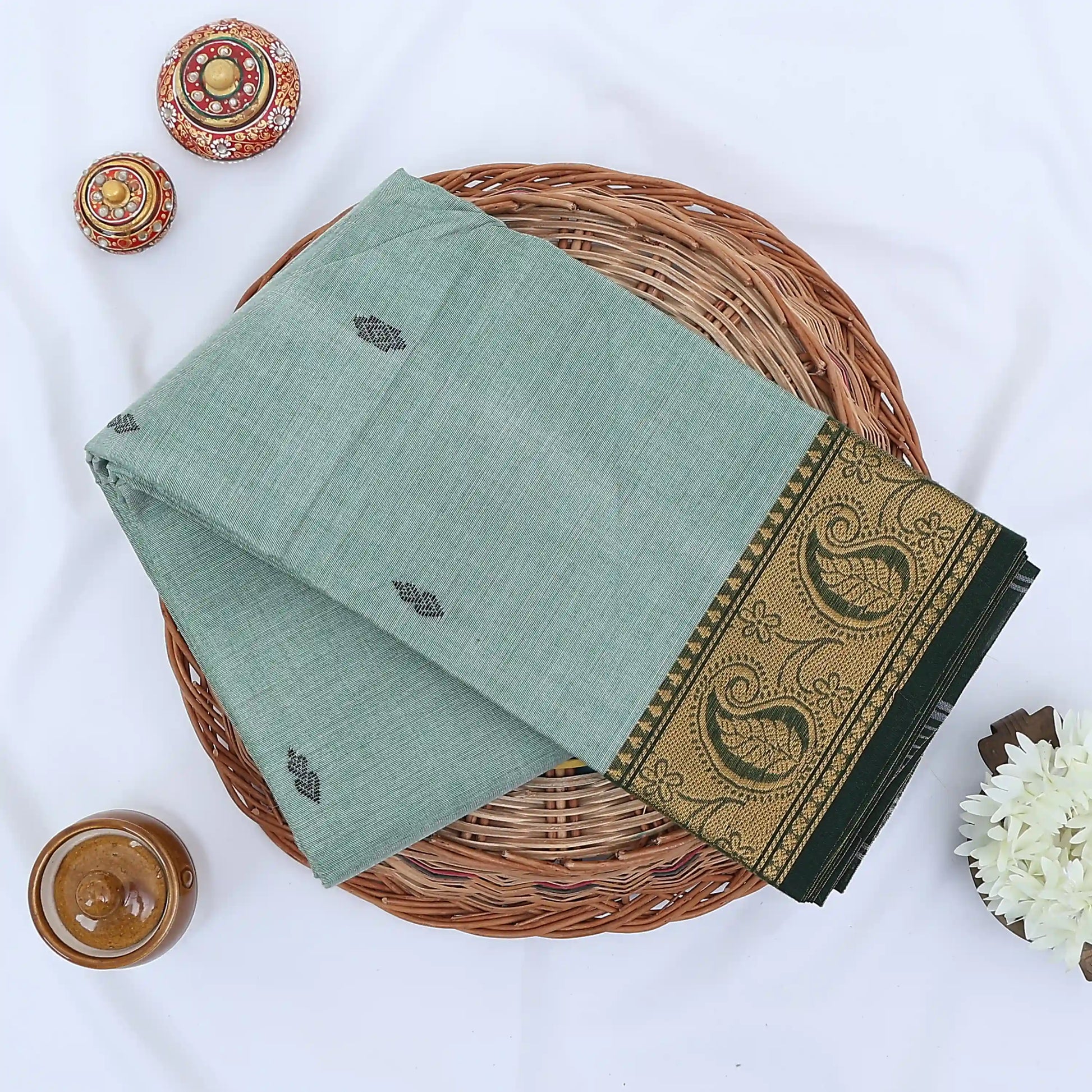 Chettinad cotton saree with light green body woven butta motifs and green paisley zari border flat lay view.