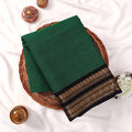 Kanchi Cotton Saree With Black And Gold Zari Border In Dark Green Folded Flat Lay View In Decorative Basket
