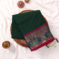Kanchi Cotton Saree With Peacock Motif Zari Border In Dark Green And Magenta Folded Flat Lay View With Floral Accents
