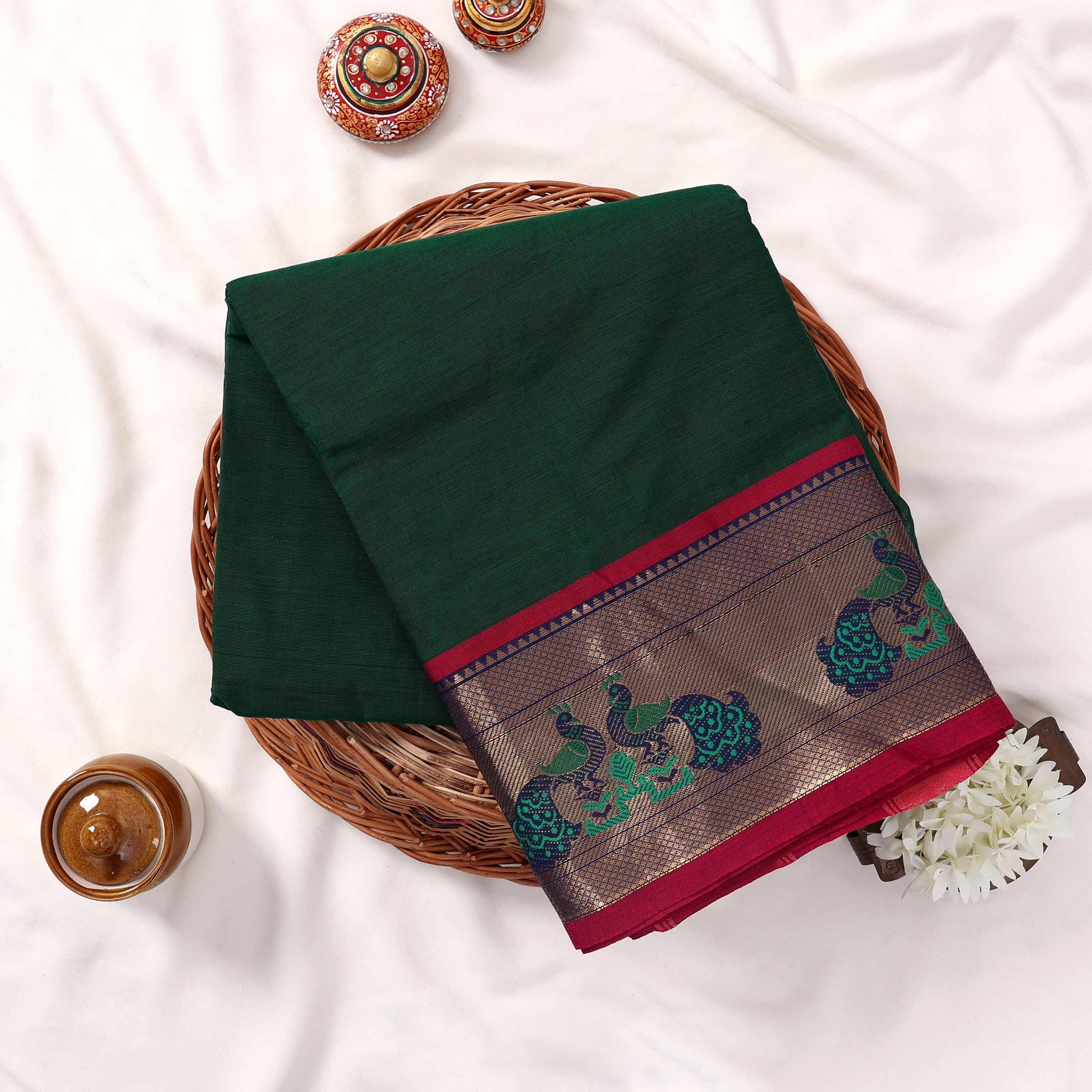 Kanchi Cotton Saree With Peacock Motif Zari Border In Dark Green And Magenta Folded Flat Lay View With Floral Accents
