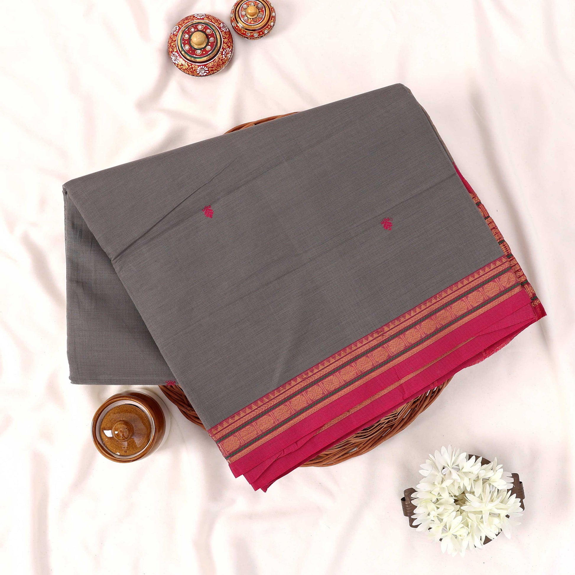 Kanchi Cotton Saree With Zari Border In Grey And Magenta Folded On Wicker Basket Top View Product Display
