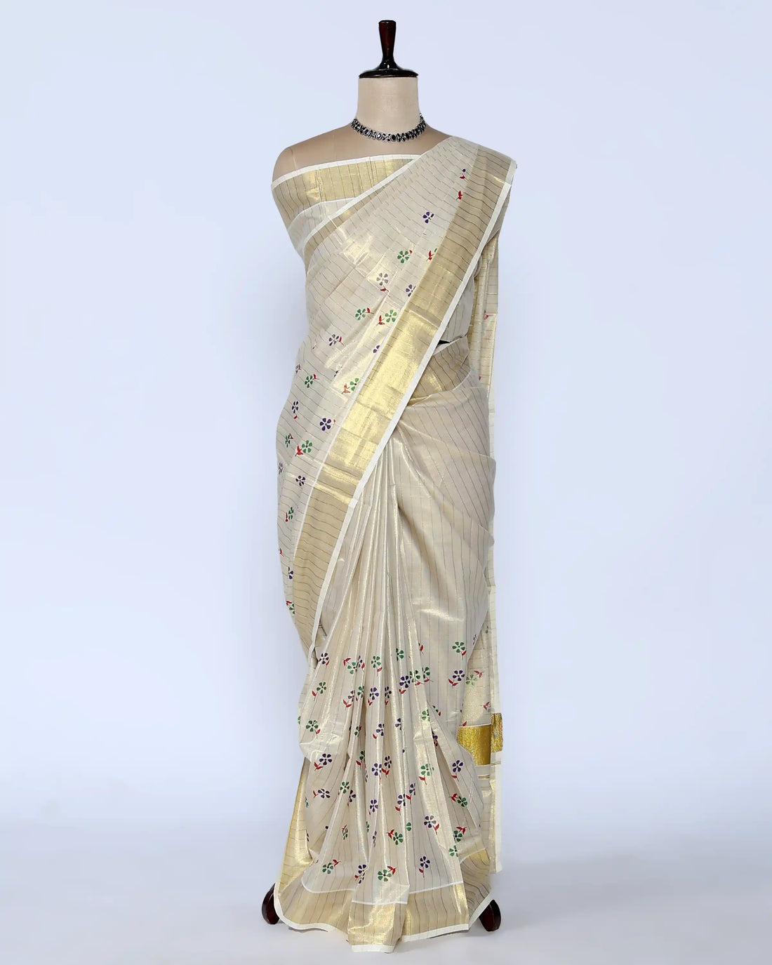A cream-colored kerala saree with gold zari stripes and small colorful floral motifs, full view
