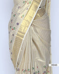A cream-colored kerala saree with gold zari stripes and small colorful floral motifs, head view