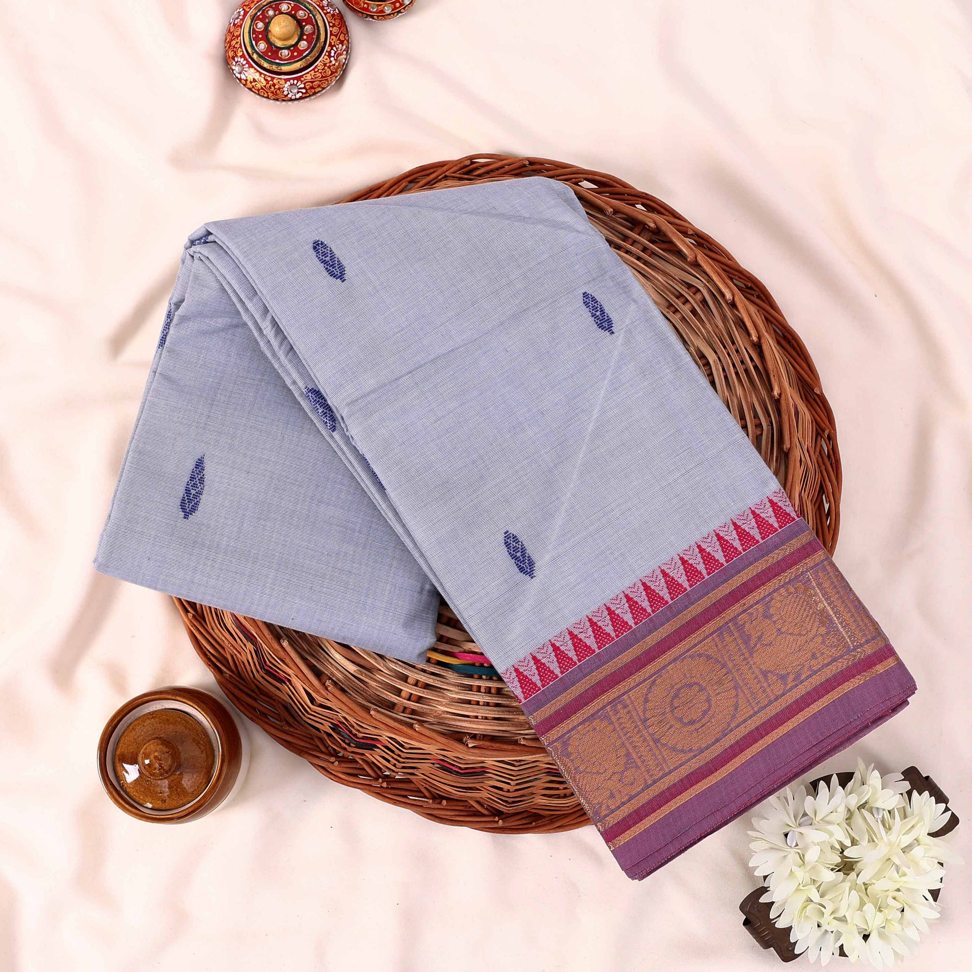 Kanchi Cotton Saree With Light Blue Body And Pink Gold Woven Border Flat Lay Top View On Woven Basket Display
