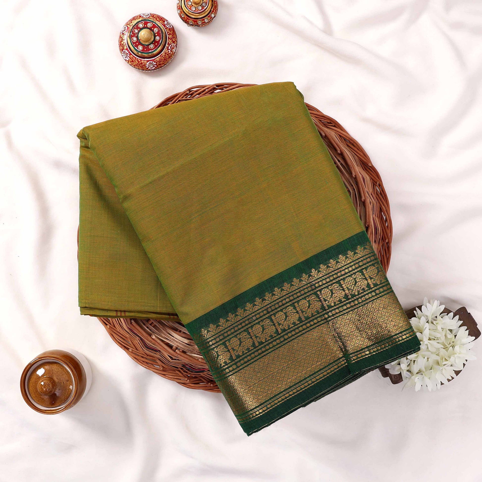 Kanchi Cotton Saree With Gold Zari Border In Light Green Neatly Folded On Wicker Basket Top View Display
