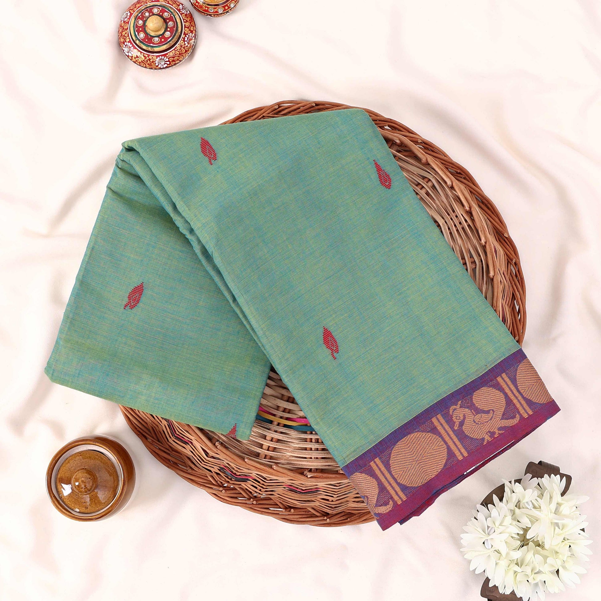 Kanchi Cotton Saree With Light Green Body Purple Zari Border And Red Butta Motifs Folded Flat Lay View With Decorative Accents
