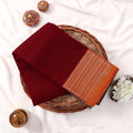 Kanchi Cotton Saree With  Maroon Body And Gold Zari Border Neatly Folded On A Wicker Tray Top View
