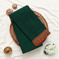 Narayanpet cotton saree with contrast woven zari border dark green folded top view on wicker basket