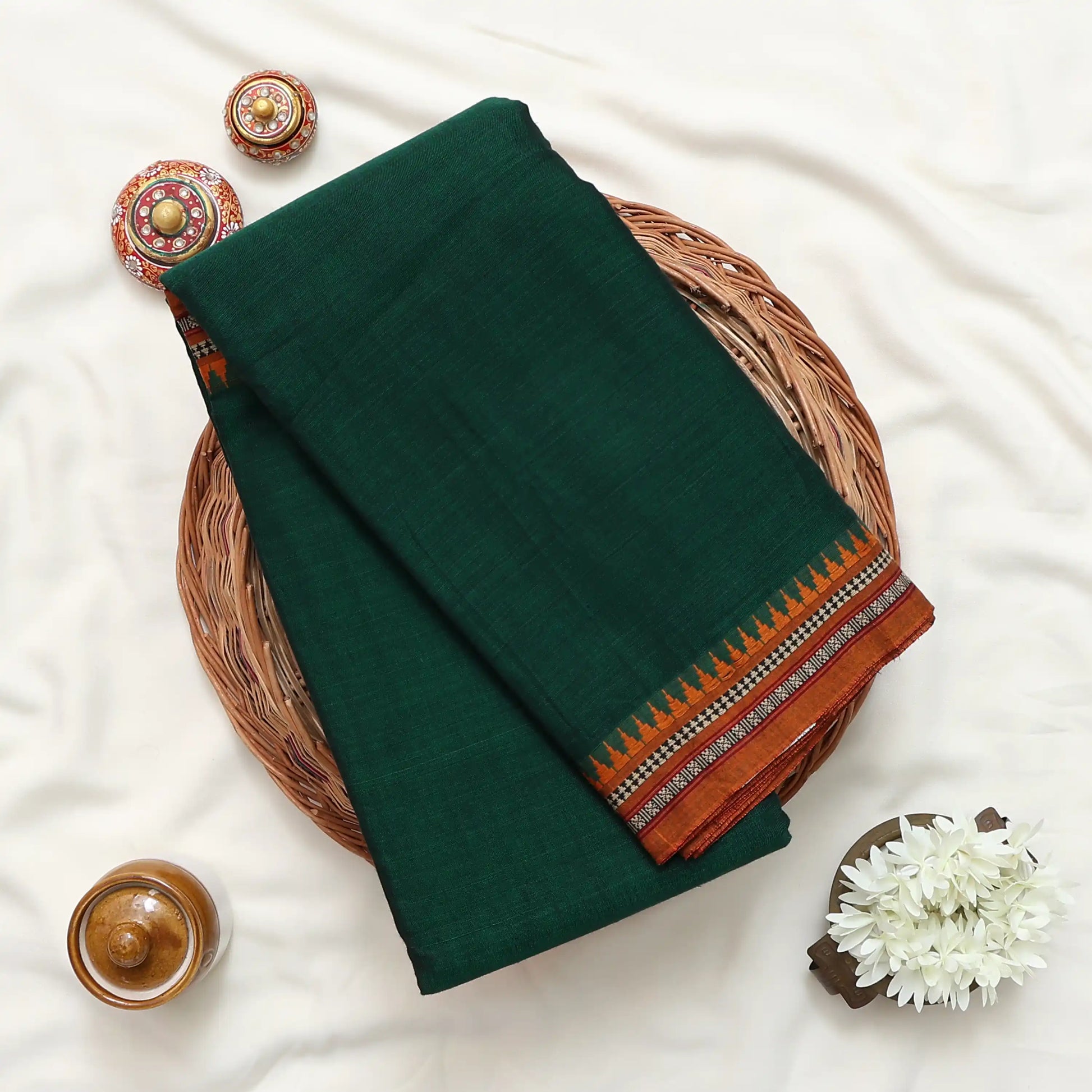 Narayanpet cotton saree with contrast woven zari border dark green folded top view on wicker basket